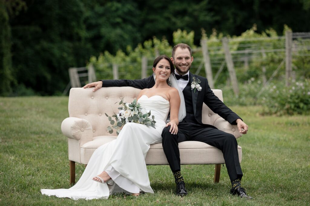 beautiful bride and groom sit lovingly on White Dahlia events Joanie Love Seat in Tabor Hill Weddings Vineyard