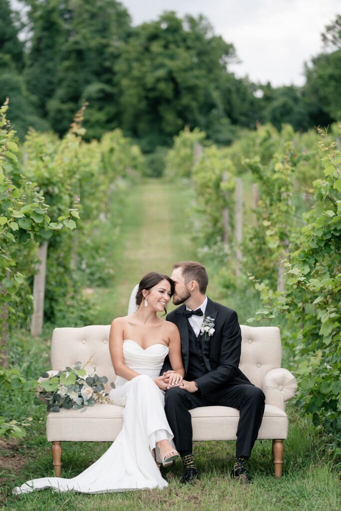 beautiful bride and groom sit lovingly on White Dahlia events Joanie Love Seat in Tabor Hill Weddings Vineyard